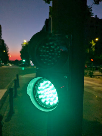 A green traffic light illuminates a deserted city street at twilight, casting a soft glow as nearby...