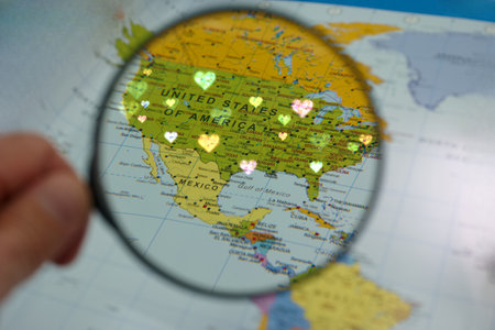 A hand holds a magnifying glass over a map where heart shapes are placed, emphasizing a playful...