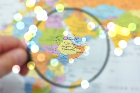 A hand is holding a magnifying glass over a colorful map highlighting Ethiopia, with vibrant bokeh...