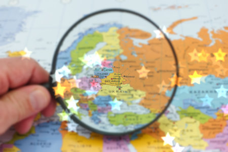 A hand holds a magnifying glass over a map highlighting Belarus among neighboring countries in...