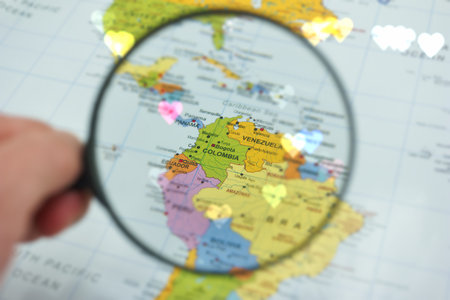 A hand holds a magnifying glass over a vibrant map of South America, with a focus on Colombia....