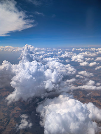 Departing from a vibrant landscape, fluffy white clouds stretch across the sky. The view captures...