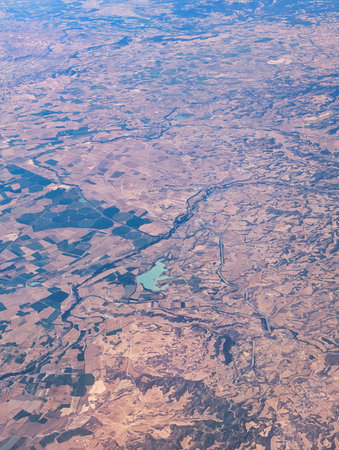 From an aerial perspective, the expansive landscape reveals a winding river cutting through patches of farmland and dry terrain in Spain.の写真素材