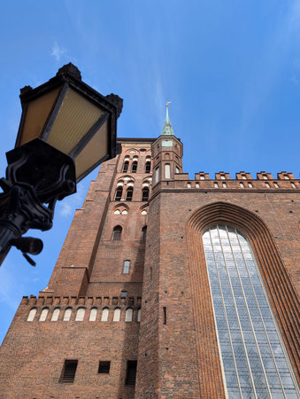 A towering brick church with a distinct steeple rises into the blue sky. A vintage lantern is...