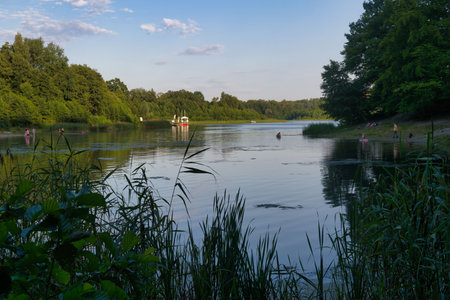 People engage in various leisure activities along a peaceful river surrounded by lush greenery under...