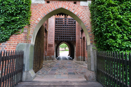 An elegant brick archway framed by lush greenery opens into a peaceful courtyard. Sunlight filters...