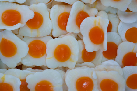 Colorful candy treats designed to look like fried eggs cover a flat surface. The bright yellow yolks...