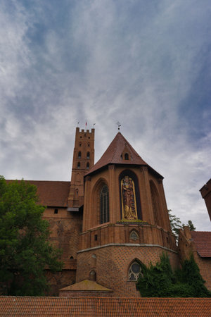Visitors admires a remarkable brick church featuring a statue, surrounded by lush greenery under an...