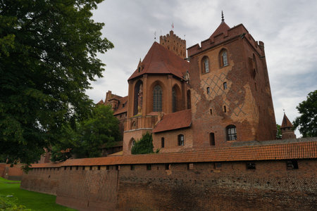 A majestic brick castle stands tall with its turrets and intricate architecture. Lush trees frame...