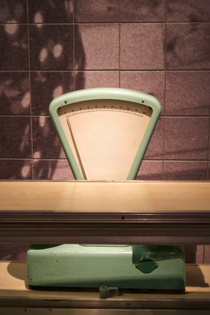 A green scale stands on a wooden counter, illuminated by soft light. The vintage design and warm...
