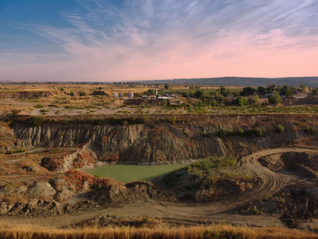 A stunning landscape shows an old mining area with layered earth formations and a green pond. The...