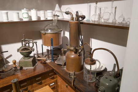 Old scientific instruments arranged in a cozy lab space. Various glassware, metal apparatus, and wooden furniture reflect a historical atmosphere of scientific exploration and experimentation.の写真素材