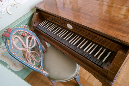 A vintage wooden piano with polished keys rests in a beautifully decorated room. Beside it, a...