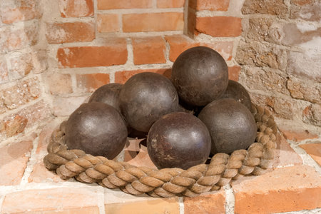 A collection of antique cannonballs is displayed on a thick rope in front of textured brick walls....
