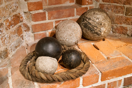 A group of five historical cannonballs in different sizes is arranged with a thick rope on rustic brick surfaces. This display is found in a museum corner, showcasing artifacts.の写真素材
