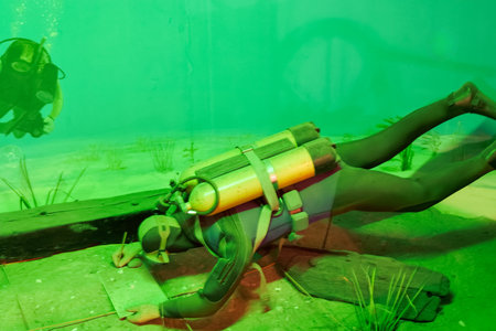 Two divers explore an underwater environment filled with greenery and remnants of a wreck. They navigate through the clear water, observing marine life nearby.の写真素材