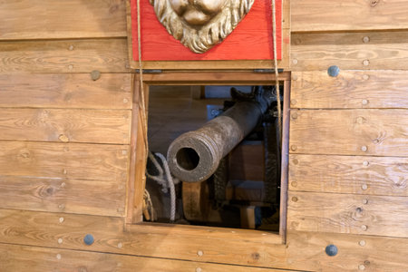 A cannon is positioned within the opening of a wooden wall in a maritime museum. Natural light illuminates the sturdy cannon, showing its historical significance and craftsmanship.の写真素材