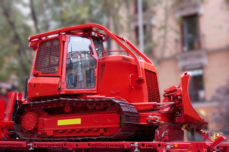A bright red excavator is parked on a city street surrounded by residential buildings. The machine is ready for construction work in the daytime, showing its machinery and design.の写真素材