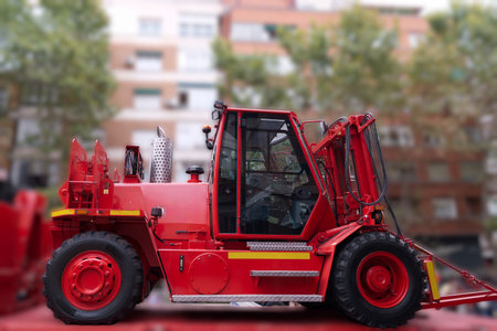 A bright red construction vehicle sits parked in a busy urban area surrounded by buildings. The machine is ready for work, showing various tools and features.の写真素材