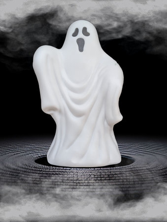 A small white ghost figure stands atop a dark, circular surface, surrounded by swirling mist. The ghost has a fearful expression, creating a spooky atmosphere at night.の写真素材