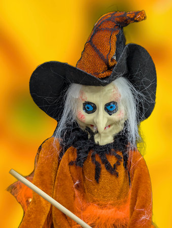 A witch doll with vibrant orange clothing and a black hat is featured. The doll has striking blue eyes and a mischievous expression, perfect for Halloween decor.の写真素材