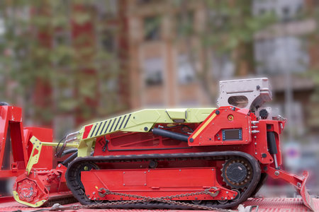 A bright red and green construction machine is parked at a construction site, with blurred buildings behind it, showcasing modern urban development during daylight hours.の写真素材
