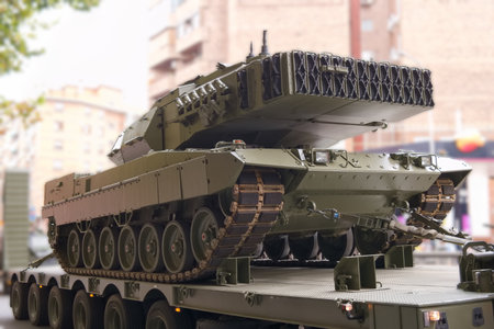 A military tank is loaded onto a flatbed truck on a city street. The vehicle is surrounded by...