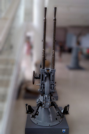 A vintage artillery piece stands on display in a spacious industrial museum. The piece is equipped...