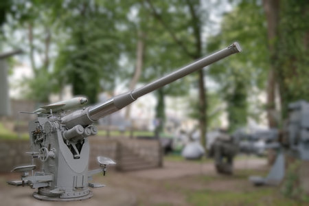 A historic artillery piece stands prominently in a park surrounded by trees and military vehicles. The scene is bright and inviting, showcasing military history on a sunny afternoon.の写真素材