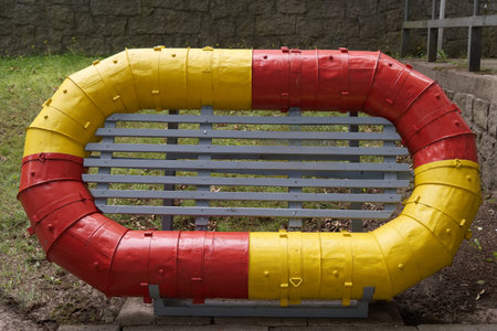 A creatively designed bench shaped like a lifebuoy is placed in a park. The bench is painted in bright red and yellow colors, adding a fun element to the outdoor area.の写真素材