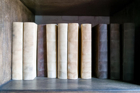 A collection of worn leather bound books stands in a wooden shelf, showing various shades of brown and beige. This cozy scene invites reading and reflection during quiet moments.の写真素材