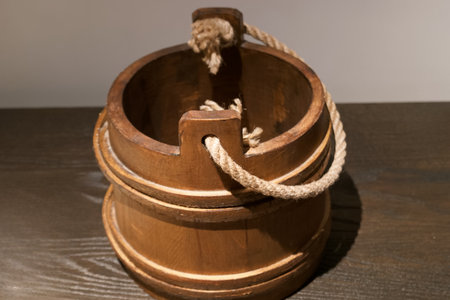 A wooden bucket with a sturdy rope handle rests on a dark wooden table, showing a simple yet rustic...