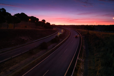 Cars travel along a curvy road as the sky glows in vibrant hues during twilight. The scene captures the peaceful transition from day to night.の写真素材