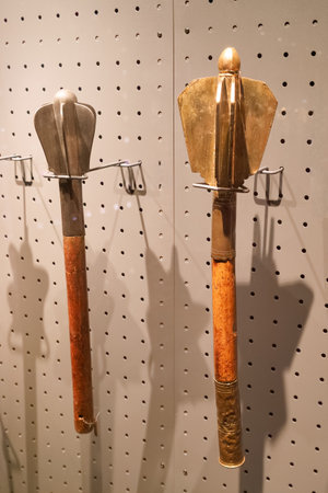 Two distinct historical tools are mounted on a display wall in a museum. Each tool features unique...