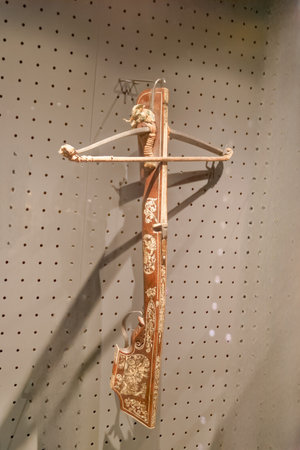 An antique crossbow is showcased in a museum, hanging against a textured wall. Its ornate carvings...