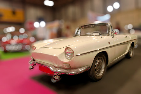 A vintage convertible car showcases its sleek design at a bustling auto show. Bright lights and...
