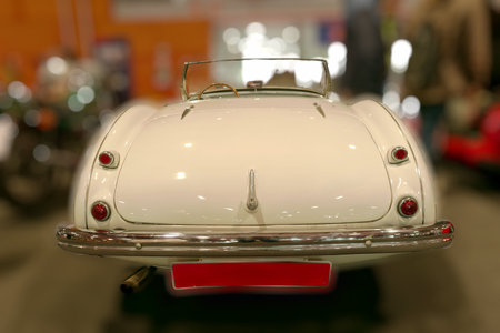 A classic white convertible car is showcased at an indoor auto show. The sleek design and polished...