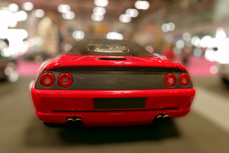 A red sports car is displayed at a car show in an exhibition hall. People are gathering around to...