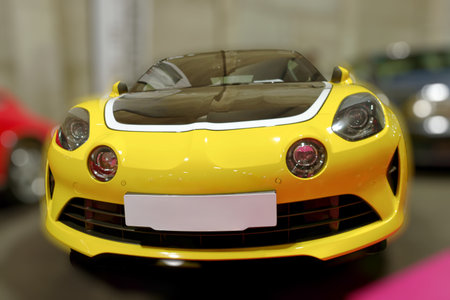 A bright yellow sports car is featured at a motor show inside a large event space. The car has...