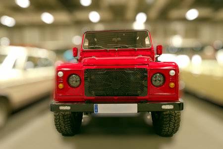 A red vehicle is parked in a large indoor space filled with other cars. The setting is bright with...