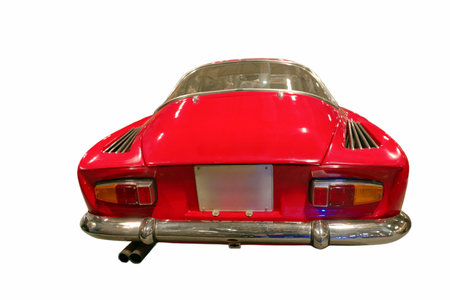 A classic red car is parked in a garage. The car has a shiny surface and a distinct rear design....