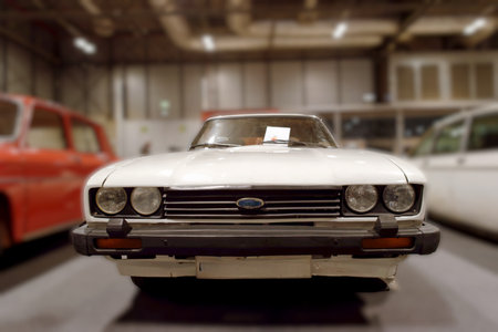 A classic car is centered in a motor museum. It has a clear view of the front with bright lights in...