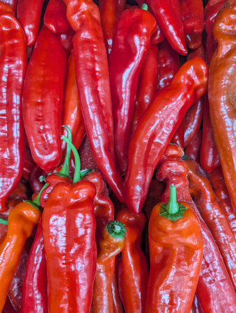 Red peppers are displayed in a market. They are stacked on top of each other in a colorful...