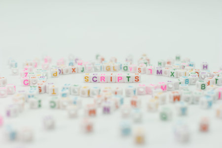 Small colorful beads with letters are scattered on a white surface. The word scripts is formed in...