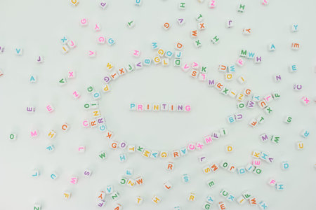 Plastic letters of various colors are scattered across a white surface. The letters form the word printing, with other letters surrounding it in a random pattern.の写真素材