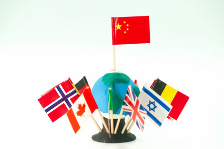 Clay globe has flags from different countries stuck in it. Flags represent China, Norway, Canada,...