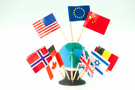 A round globe sits on a plain surface. Various flags representing countries are placed around the...