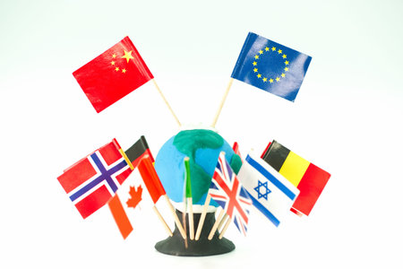 A globe made of clay is surrounded by various country flags. The flags stand on wooden sticks, showing different nations. This display is part of a learning tool in a classroom setting.の写真素材