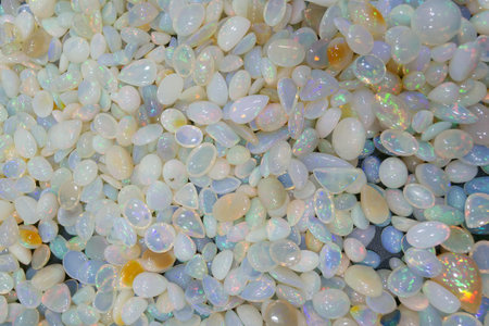 A large number of opal stones are spread out on a flat surface. The stones are smooth and display...