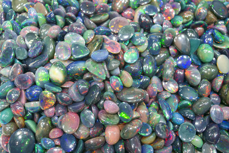 Bright polished stones cover a table at a market. Various colors and shapes blend together. Sunlight...